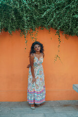 Fototapeta premium A woman in a long dress is standing in front of a wall with green vines