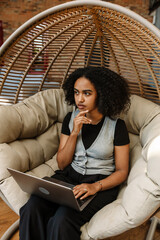 A female worker looks thoughtfully in front of her and holds a laptop while sitting in a cocoon...