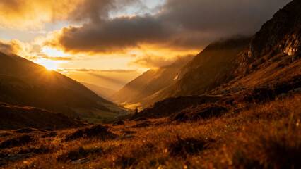 Naklejka premium Golden sunrise illuminates a mountain valley with dramatic clouds and warm light