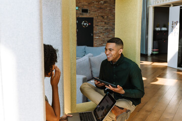 Male worker holding a computer tablet and laughing while listening to a female worker holding a...