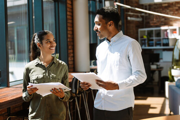 Male and female employees holding documents and smiling while standing and talking