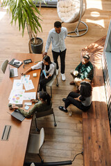 A male worker stands next to a group of four workers sitting at a table and on a bench