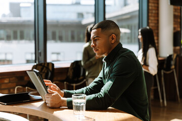 A male worker sits at a desk and types on a computer tablet