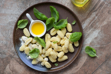 Plate with uncooked italian gnocchi on a brown granite background, horizontal shot, view from above