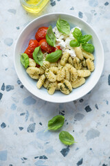 Potato gnocchi with ricotta, roasted tomatoes and fresh basil, vertical shot on a white and blue granite background, flat lay