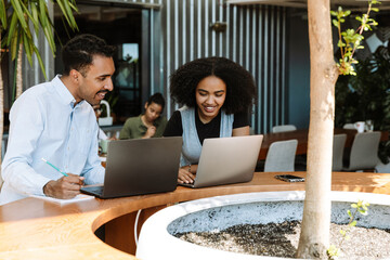 Male and female workers are laughing and looking at laptop while sitting at the table