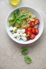 Components for caprese pasta salad with farfalle, vertical shot on a beige stone background, top view