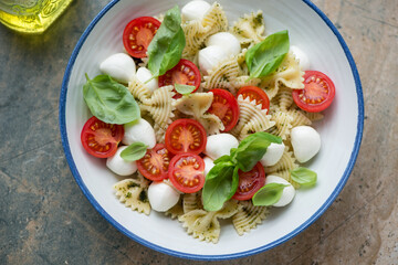Plate of caprese pasta salad with mini mozzarella balls, cherry tomatoes, farfalle and basil, horizontal shot, elevated view