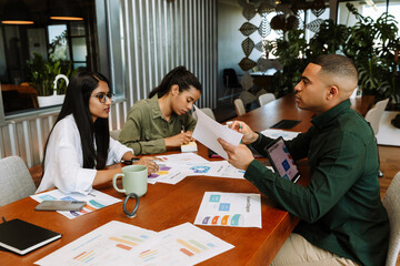A male worker holds a document and sits at a table opposite two female workers