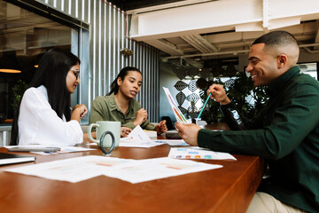 Fototapeta premium A male employee laughs and looks at documents while two female employees sit across from him at a table