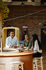 A male worker laughs and listens to a female worker with a female worker while they sit at a table