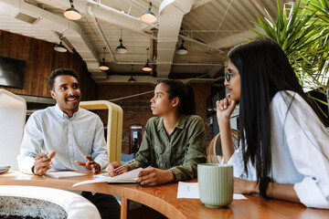 Two female employees listen to a male employee sitting next to them at the table