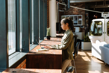 A female worker is typing on a laptop and standing at a table