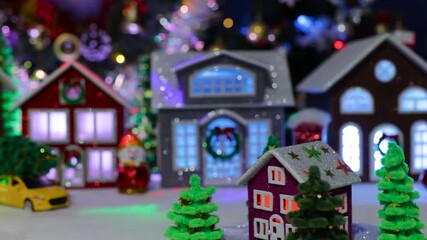 A close-up of a dark pink house surrounded by Christmas trees rotating in the center of a large decorated Christmas town