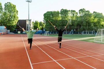 Two men stand on one leg and hold crutches in their raised hands