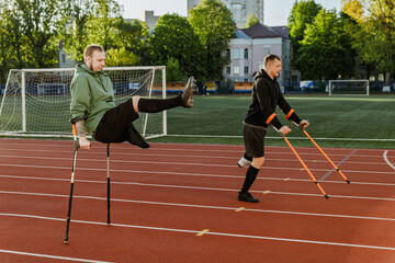Two men walk on crutches while one of them raises his leg