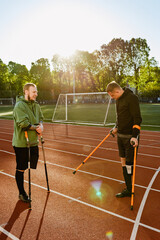 Obraz premium Two men talking and standing on a running track while holding crutches