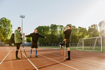 A group of three men are stretching their arms while two of them are leaning on crutches with their...