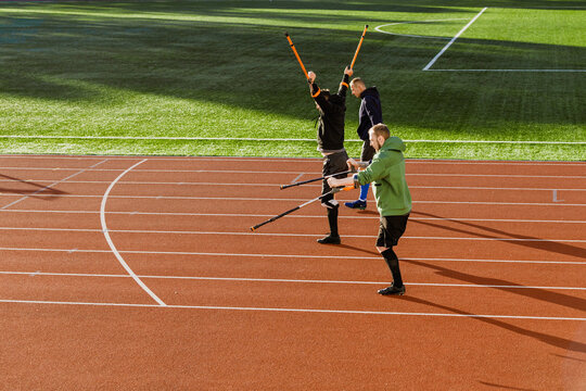 Two men stand and hold crutches up and in front of them while a man walks next to them - Powered by Adobe