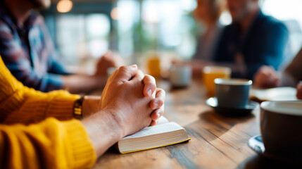 Hands clasped in prayer position around table with open books coffee cups visible support group meeting faces not shown faith community gathering mental health prayer support
