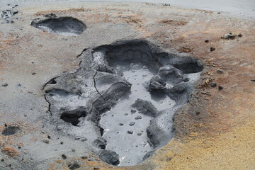 dark gray mud bubbling in a hot mud pot, the surrounding soil covered in yellow and ochre sulfuric...