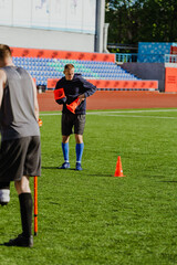 A man holds soccer cones and stands next to a man on crutches