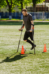 Fototapeta premium A man dribbles a ball between cones while leaning on crutches with his hands