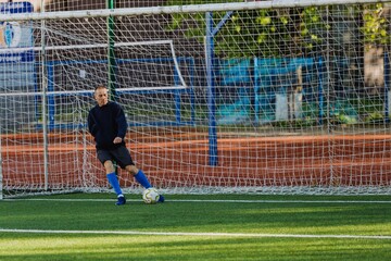A male goalkeeper kicks the ball while standing in front of the goal