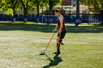 Obraz premium A man walks and dribbles a ball across the field with a crutch