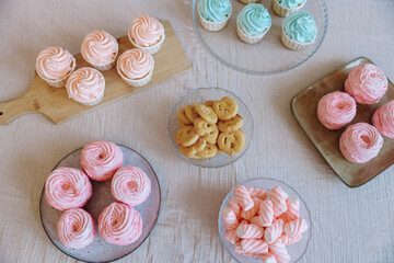 Overhead view of a dessert table featuring pink and mint cupcakes, round pink marshmallows,...