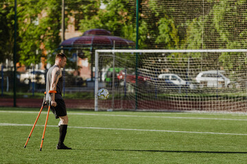 A man looks at a ball in front of him and stands while holding crutches
