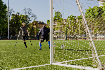 A man on crutches looks at the ball which is near the man on the side of the goal