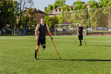 Two men stand and hold crutches while one of them looks up