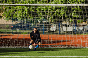 A man stands in the goal and catches the ball in front of him