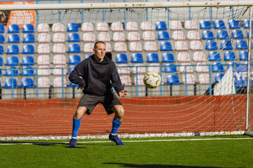 A man stands and holds out his hand to catch a ball flying towards the goal