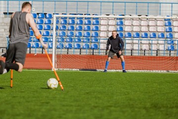 A man stands and looks at a man on crutches who is swinging to kick the ball into the goal