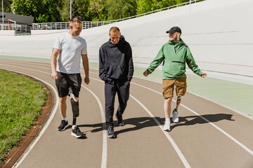 A group of three men talk and laugh as they walk along a running track, two of them in prosthetics