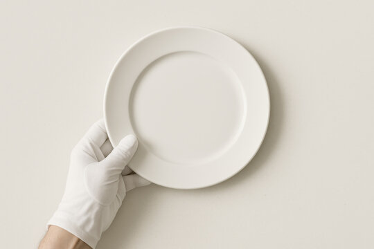 Minimalist Presentation: An isolated hand in a pristine glove delicately holds a clean, empty plate, inviting the viewer to envision the endless culinary possibilities