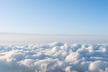 Naklejka premium Arial view from the airplane window shows a vast white cloudscape under a bright blue sky, resembling a heavenly landscape above the horizon