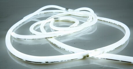 Bright white neon flex coil. Smooth plastic casing, illuminated interior. Simple studio shot, clean background. Lighting emphasizes curves, modern design.