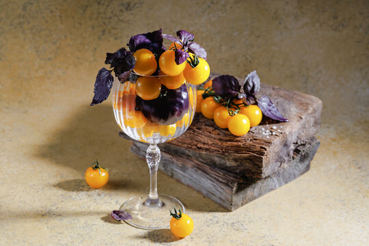 Glass filled with yellow cherry tomatoes and purple basil on textured wood and stone surface in natural light