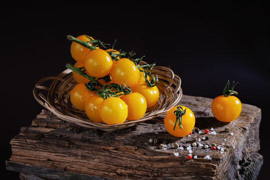 Yellow cherry tomatoes with water drops in wicker bowl on old wooden surface with spices