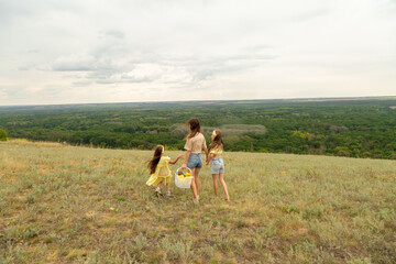 Naklejka premium Family on a meadow, mother and daughter holding hands while carries picnic basket