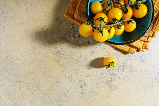 Yellow tomatoes on vine in rustic blue bowl with space on the side for text and design