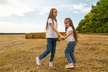 Fototapeta premium Children run on the mown wheat field where there are sheaves.