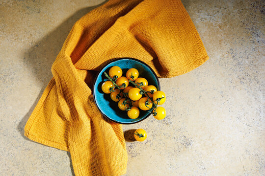 Top down view of fresh yellow cherry tomatoes in rustic blue bowl with yellow cloth and space for text - Powered by Adobe