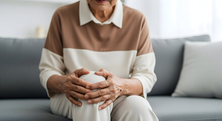 Elderly Woman Suffering from Knee Pain While Sitting on Sofa, Highlighting Joint Discomfort and Senior Health Issues