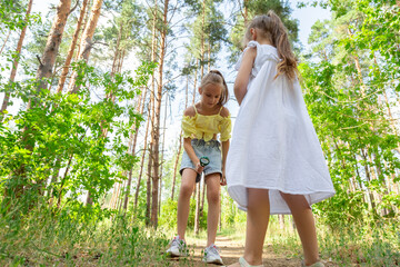 Fototapeta premium Children with magnifying glass exploring the nature outdoors. Little girls playing in the forest with magnifying glass on a sunny day in forest