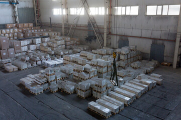 Stacks of aluminum ingots on pallets in a large industrial warehouse or foundry. A concept of the metallurgical industry, raw materials, and heavy manufacturing.