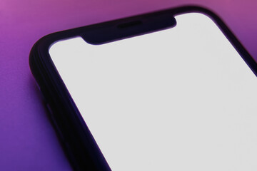 Close up of smartphone with empty white display lying on gradient pink purple backdrop, modern digital design concept for technology or web banner use. Phone mock up 